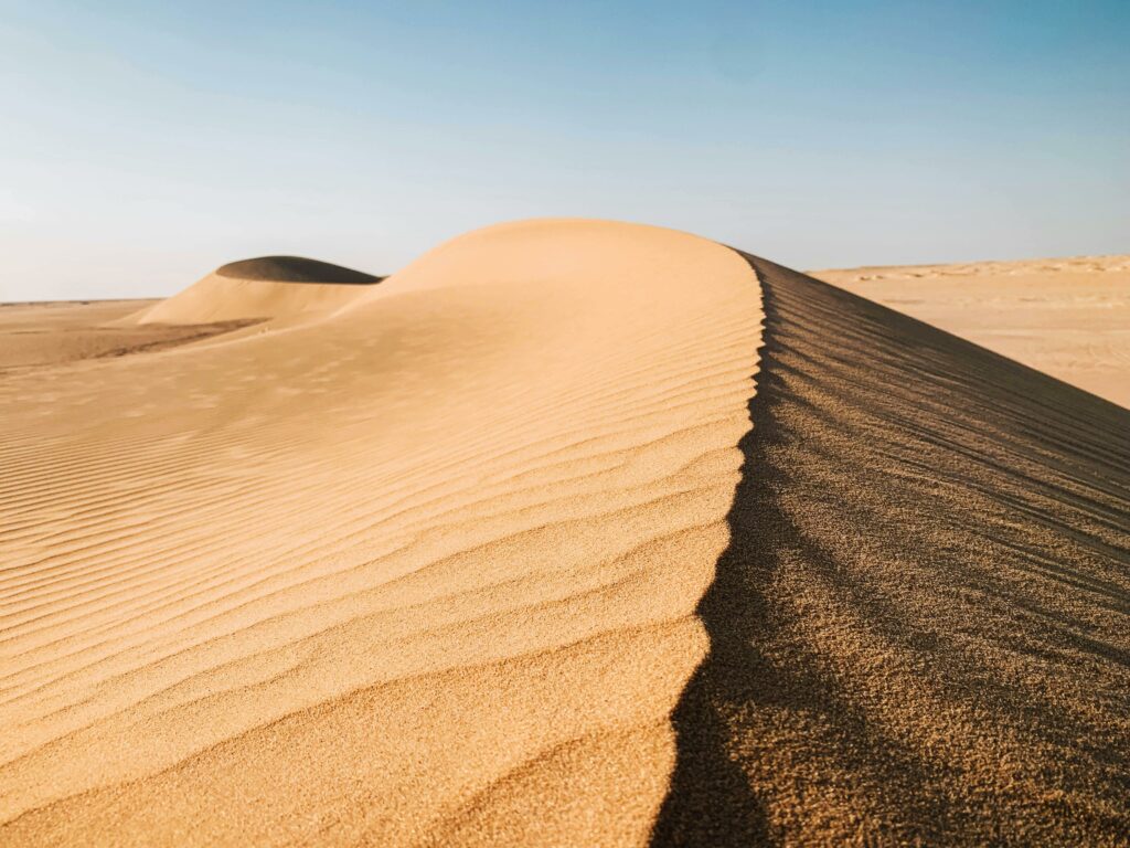 Golden sand dunes stretch under a clear blue sky, capturing the essence of arid landscapes.