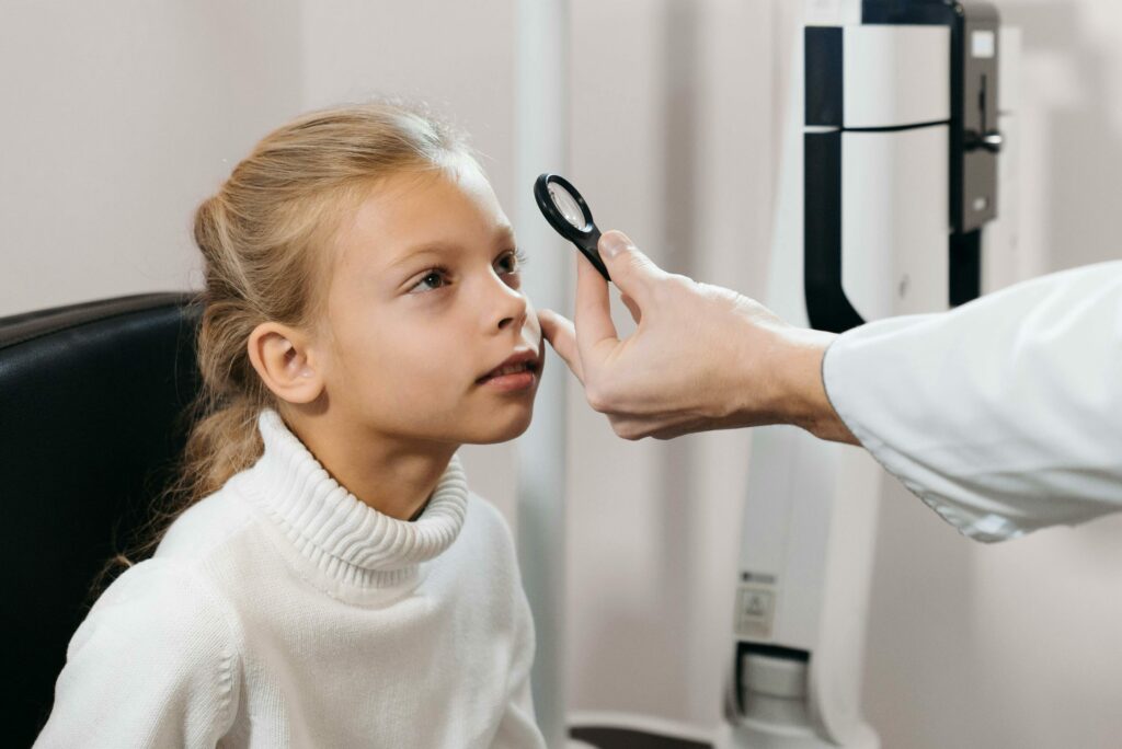 Caucasian girl undergoing an eye exam by a professional in a clinical setting.